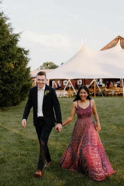A newlywed couple holding hands and walking on a lawn