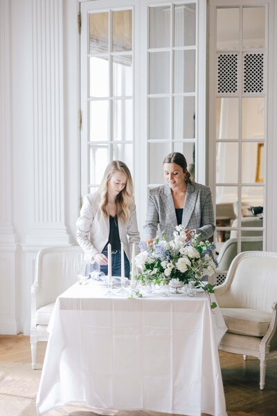 two girls create a wedding flat lay for an elegant couple in a light and airy room