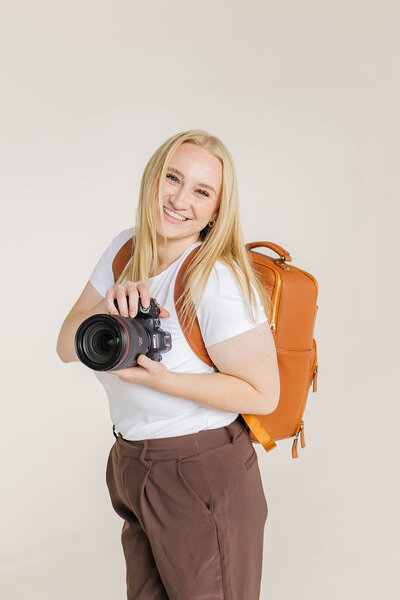 Jessica Nicole Photography smiling holding a camera and wearing a stylish camera backpack, ready to capture your Colorado wedding.
