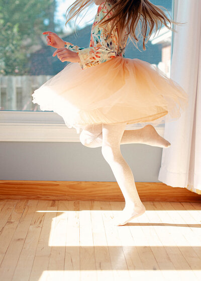 A girl twirling in a pink skirt in a sunpatch in her home