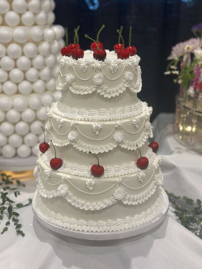 A white, three-tiered cake with ornate piping and red cherries as decorations. Representing Cakes By Blythe vendor profile for the Crush Collective wedding show.