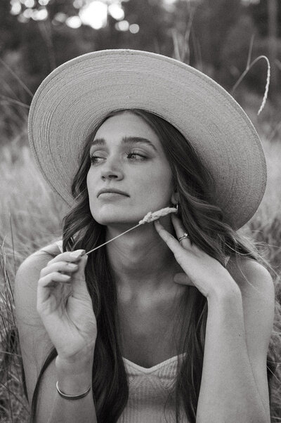 A close up portrait of Showit and Shopify designer, Rosa, wearing a straw hat and daintily holding a piece of grass