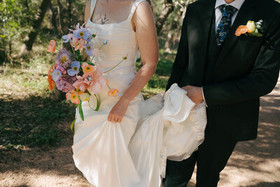 A bride and groom walking after their wedding ceremony in Austin, Texas. The bride is holding her flowers, the groom is holding her dress. 