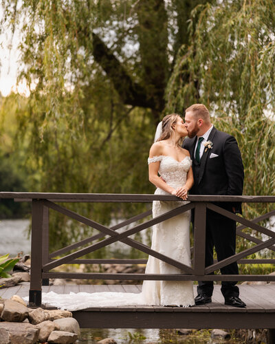 The bride and groom sharing a kiss on the bridge at Old Daley on Crooked Lake in Averill Park, NY.
