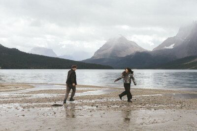 couple run along a beach laughing with misty mountains in the background