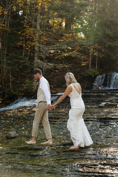 bride and groom standing together with a waterfall in the background and green trees