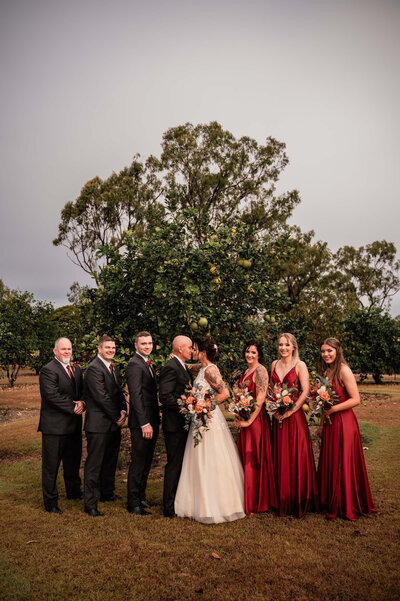 A wedding party dressed in elegant red dresses and classic tuxedos, celebrating a joyful wedding together.