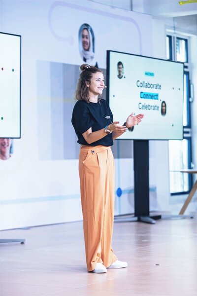 Moderatorin Hanna Zöller auf Bühne bei Business-Event, mit Präsentation im Hintergrund – professionelle Moderation für Unternehmen