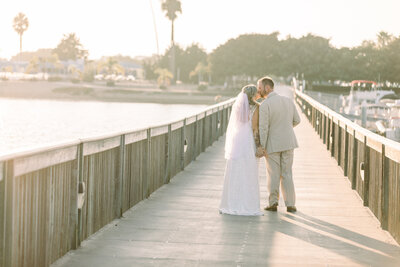 Bride and Groom stop for a kiss as they walk along a bridge overlooking the Newport Back Bay