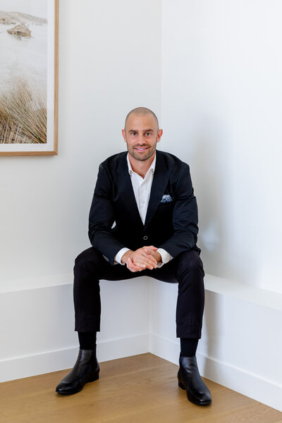 Jon Moses leaning against a wall  wearing a suit, and holding an iphone. black and white photo