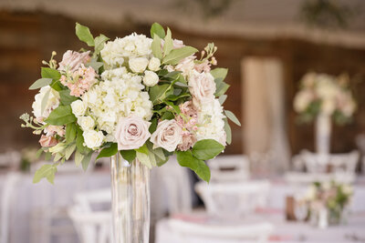 Tall wedding centerpiece with white hydrangeas, blush roses, and lush greenery in a glass vase