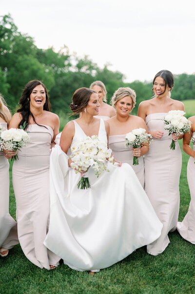 outside of minneapolis minnesota wedding bride and bridesmaids smile candidly together while holding neutral tone bouquets