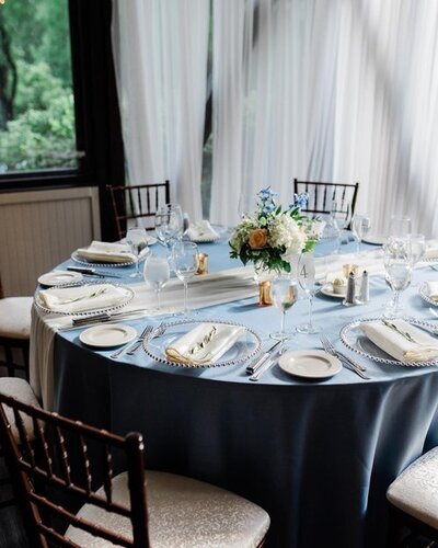 table with blue table cloth, white plates, and a vase of flowers on it