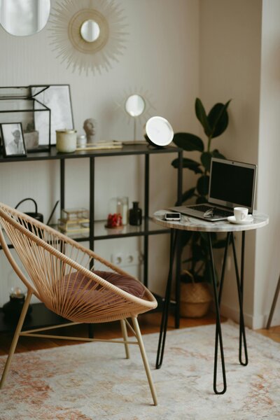 Modern home office setup with a woven chair, small table, and open laptop, illustrating a comfortable and productive remote work environment.