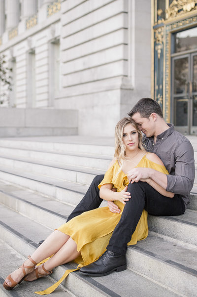 young engaged couple sitting on the steps of San Francisco City Hall