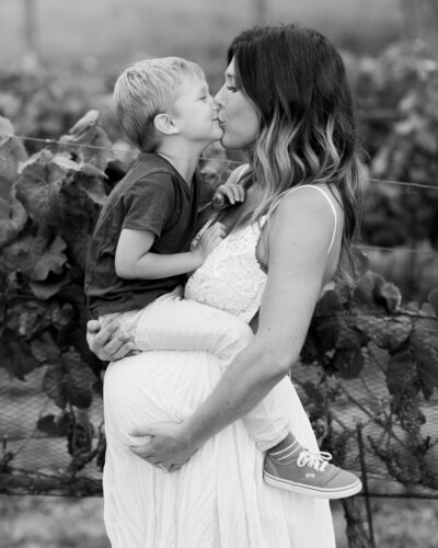 Pregnant mom and toddler son kissing in Carmel Valley Ranch vineyard