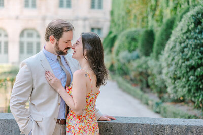 Couple smiling at each other, about to kiss, with the woman’s hand resting on the man’s chest during a romantic Paris photoshoot at Hôtel de Sully in the Marais.