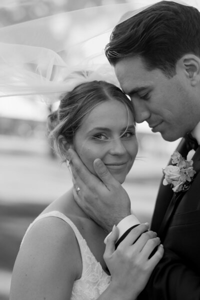 black and white image of a married couple embracing under a veil 