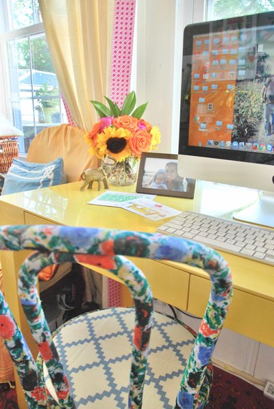 A floral chair in front of a yellow computer desk.