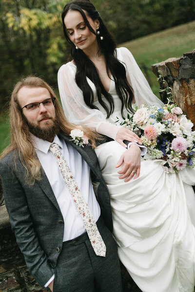 bride sits on a wall looking down at groom