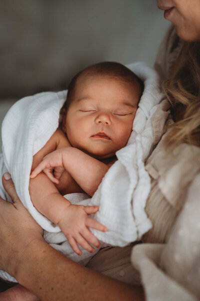 Newborn baby sleeping peacefully in a neutral swaddle during an in-home session