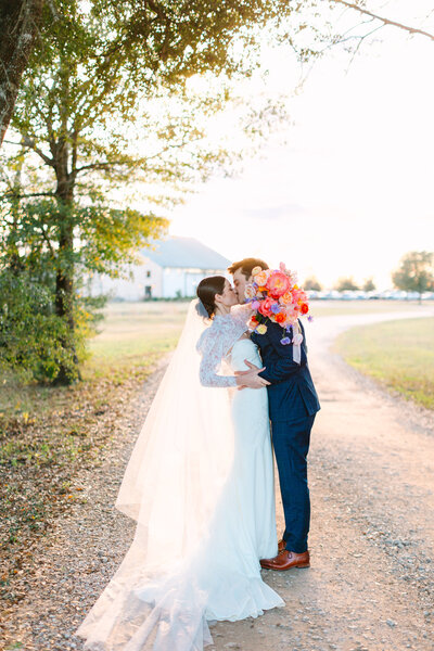 Bride and groom kissing on a dirt road with venue in the background