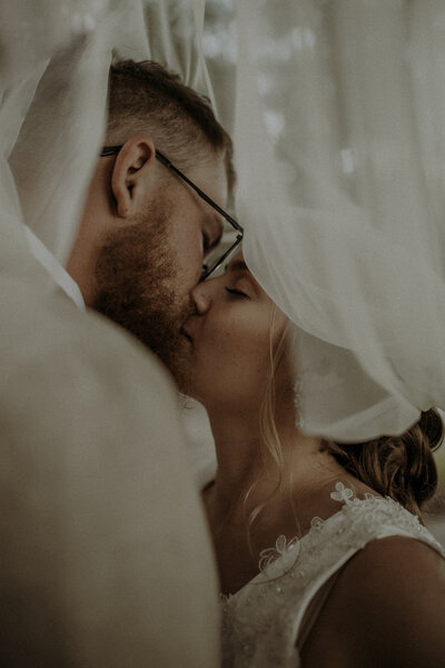 Bride and groom kissing under the bride's veil.