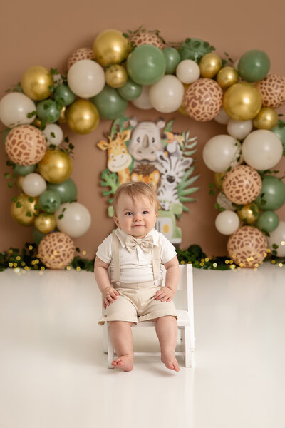 little boy in khaki outfit with bow tie and jungle backdrop