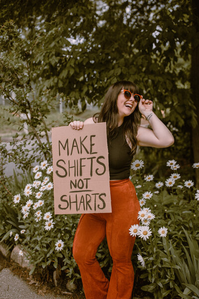 Ashley Mae Fernandez holding up a sign with slogan "make shifts not sharts"