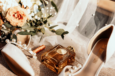 Burberry goddess perfume bottle with white heels with a pearl strap and the brides bouquet set in the church pew of Mildred B Cooper Chapel in Bella Vista, AR