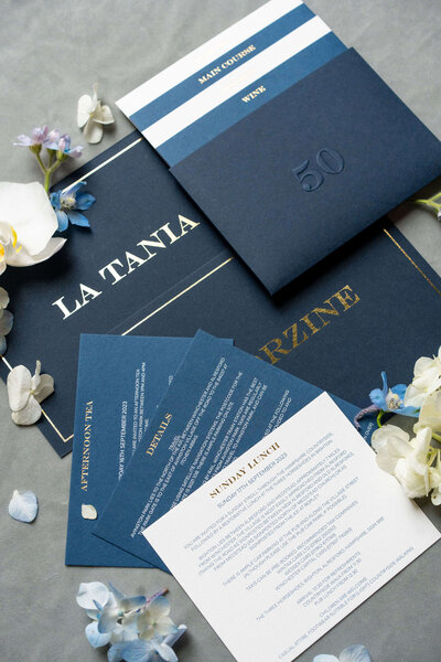 flatlay display of blue stationery for a birthday party including table names and menus with flowers scattered around