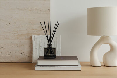 na třech knihách stojí tyčinkový aroma difuzér a vedle toho stojí designová lampa