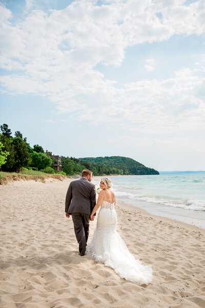 newlywed couple on beach holding hands with bride looking back over shoulder