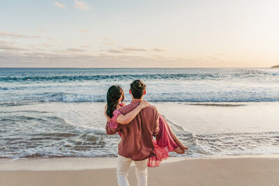 man carrying wife in arms on beach