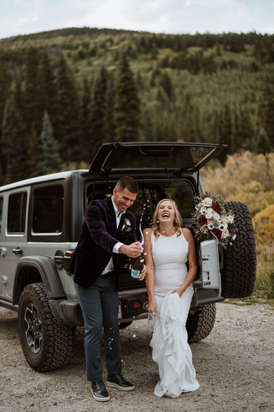 Newlyweds pop champagne by Jeep after Breckenridge wedding, captured by photo and video elopement team.
