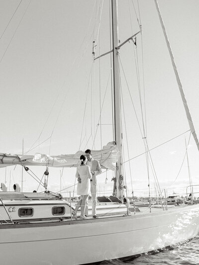 Black and white engagement photo of a bride-to-be and groom-to-be on the deck of a sailboat that is on the Atlantic Ocean