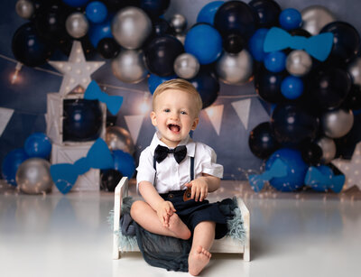 one year old boy sitting in white bed for cake smash photoshoot