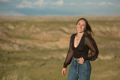 Amy standing in a field at golden hour wearing high-waisted denim and a sheer blouse, representing grounded creativity and soulful branding connection