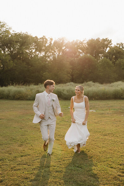 A bride and groom running through the field at sunset The Era Wedding & Event Venue