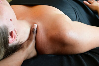 Massage Therapist performing a lower neck and shoulder massage on client face up on massage table