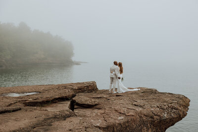 bride and groom embracing and kissing on a rock overlooking lake superior