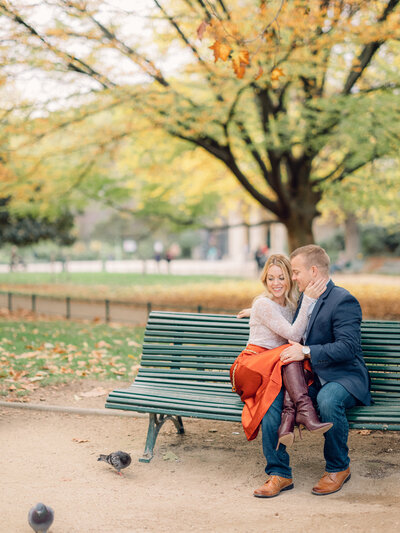 a couple citting on a bench and snuggling up together at parc monceau in paris during the autumn