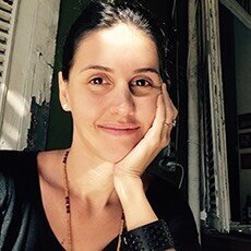 Larissa has dark hair pulled back and her hand on her cheek