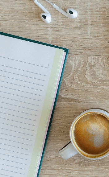 Open notebook and coffee at a table with earbuds, suggesting focus and connection in a work setting.