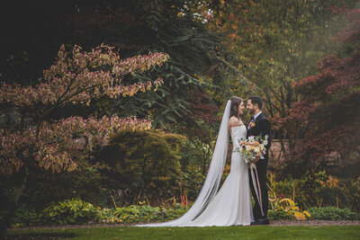 Bride and groom share romantic moment in garden, flowers created by the little flower hut