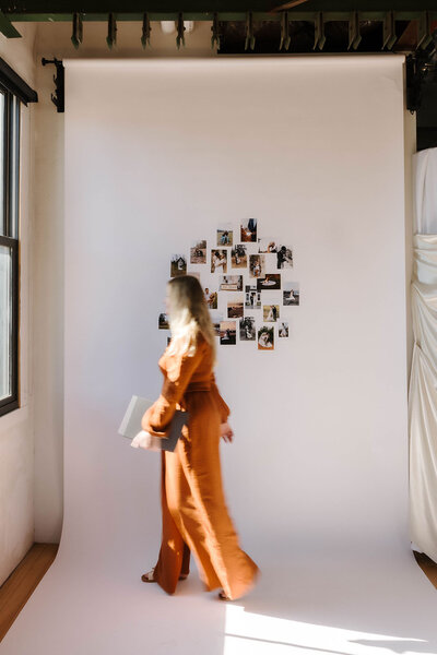 Travel elopement photographer walks with her work displayed in the background, showcasing moments from past adventures.