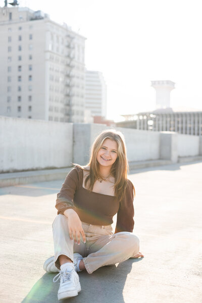 Beautiful girl sitting on top of a rooftop smiling at camera taken by Spokane Senior Photographer