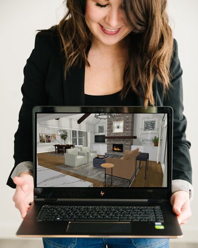 A woman holding a laptop displaying a virtual living room