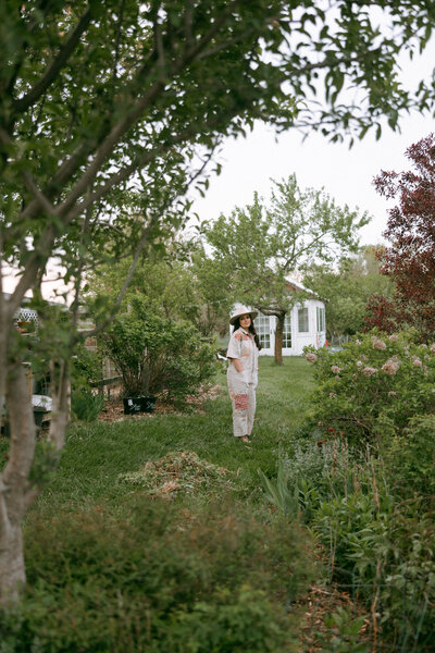 woman standing in backyard cottage garden surrounded by greenery and soft spring blooms

