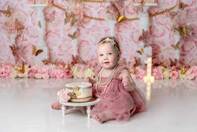 Birthday girl celebrates with a cake smash on a pink and gold rose background